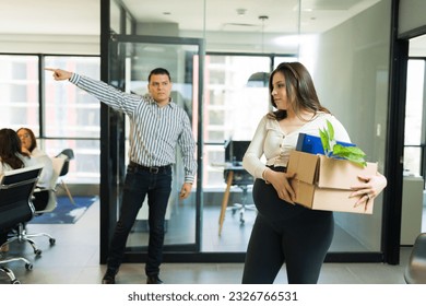 Upset mid adult male employer pointing at door while firing a pregnant female employee for bad work in office - Powered by Shutterstock