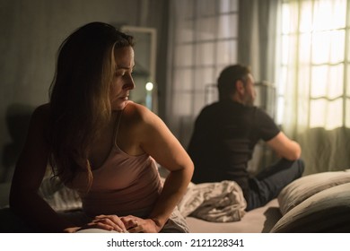 Upset mid adult woman with her husband in bed hehind her, relationship problems concept.