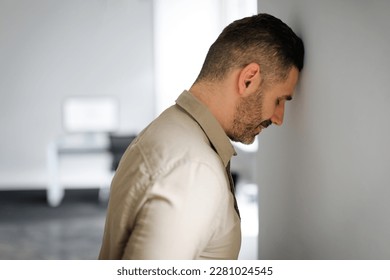 Upset middle aged businessman banging his head against wall in despair looking stressed, having problems at work. Business failure, unsuccessful negotiations, failed job interview concept