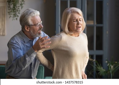 Upset Middle Aged Mature Woman Touching Back Feel Sudden Low Lumbar Backpain At Home, Elder Husband Helping Senior Wife Having Spine Injury Osteoporosis, Old Couple Support In Health Problem Concept