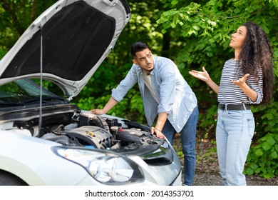 Upset Middle-eastern Couple Having Broken Car While Countryside Trip, Puzzled Arab Guy Checking Engine, Emotional Brunette Lady Looking Up, Sad Mixed Race Family Stuck In The Middle Of Road