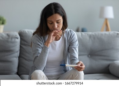 Upset millennial girl sit on couch in living room feel frustrated with bad news pregnancy test results, sad distressed young woman confused with infertility issues, female health problem concept