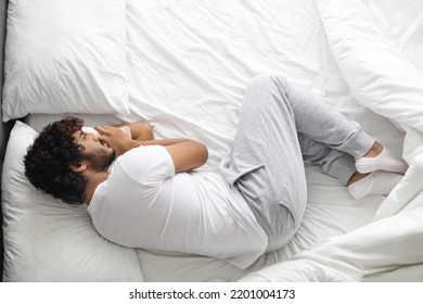 Upset millennial hindu guy in white pajamas lying on bed at home, feeling down, experiencing troubles, top view, looking at empty bed space by him. Depression, loneliness concept - Shutterstock ID 2201004173