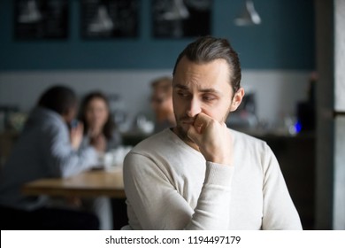 Upset millennial outsider feel offended lack company, young outcast guy suffer from discrimination, jealous of friends hang out together in café, envious male loner depressed sit alone in coffeeshop