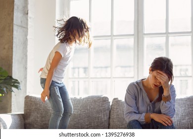 Upset mother having problem with noisy naughty daughter jumping on couch and screaming, demanding attention, frustrated mum tired of difficult child, child tantrum manipulation concept - Shutterstock ID 1395276938