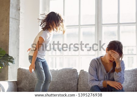 Upset mother having problem with noisy naughty daughter jumping on couch and screaming, demanding attention, frustrated mum tired of difficult child, child tantrum manipulation concept
