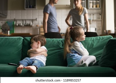 Upset offended toddler brother and sister sitting separately on couch, sofa with arms crossed, little girl and boy ignoring each other, not talking, puzzled parents discuss situation - Powered by Shutterstock