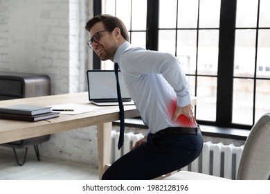 Upset Office Manager Touching Painful Back And Standing Up At Desk. Young Business Man Feeling Backache, Suffering From Sedentary Work Disease, Fibromyalgia, Rheumatism. Health Problem Concept