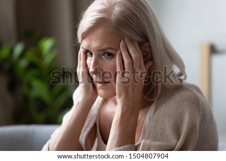 Upset older woman touching temples, feeling bad, pressure, sitting alone, mental disorder or dementia, frustrated mature female looking in distance, thinking about emotional or health problem