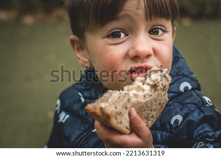 Upset poor hungry kid is eating bread. Homeless with dirty face. Portrait of child boy with big eyes. Crisis, peace, stop aggression, War in Ukraine. Sad refugee. Face asking for food.