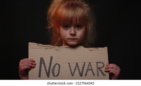 Upset poor toddler girl kid homeless with dirty face protesting war conflict raises banner with inscription massage text No War on black background. Crisis, peace, stop aggression, child against war