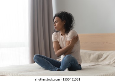 Upset sad African American woman sitting in bed alone, hugging herself, feeling lonely, unhappy girl has psychological troubles, trauma, thinking about problem in bedroom, unwanted pregnancy - Powered by Shutterstock