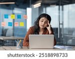 Upset and sad woman reading email, businesswoman looking at laptop screen with hand on head, thinking and worried, female worker inside office at workplace.