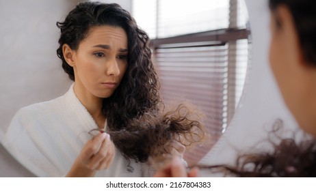 Upset sad young woman distressed by damaged hair frustrated about split ends girl worried about loss brittle dry hair hormone problem vitamin deficiency reflecting in mirror haircare treatment concept - Powered by Shutterstock