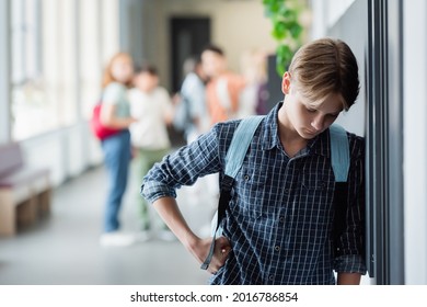 upset schoolboy standing alone with bowed head near blurred pupils in school corridor - Powered by Shutterstock