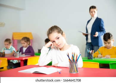 Upset Schoolgirl Sitting At A Desk In Classroom Elementary School