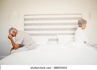 Upset senior couple sitting on the opposite ends of the bed after a fight - Powered by Shutterstock