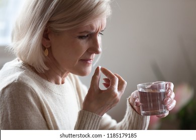 Upset Senior Ill Woman Holding Pill And Glass Or Water Taking Painkiller Medicine To Relieve Headache Pain, Sad Middle Aged Elderly Lady Worried About Side Effects Of Meds For Old Person Concept