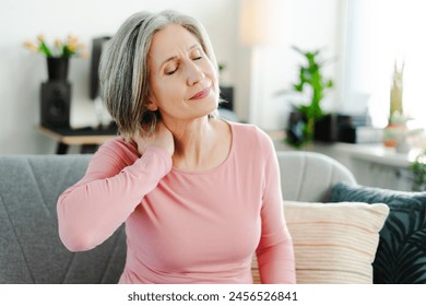 Upset senior woman having neck pain, sitting at sofa at home, with closed eyes. Health care concept - Powered by Shutterstock