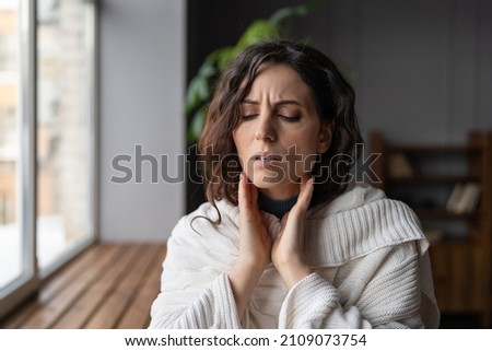 Upset sick woman standing at home touching swollen glands, having pain or scratchy sensation in throat, selective focus. Female suffering from angina or tonsillitis caused by infection or irritation
