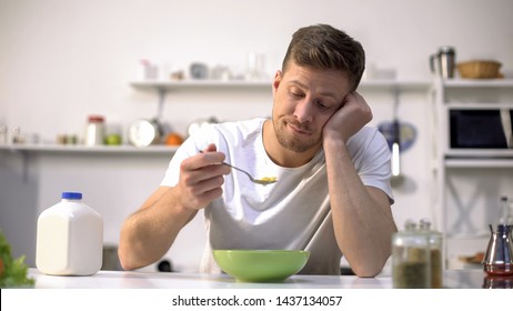 Upset single man eating tasteless cereals for breakfast, lack of appetite