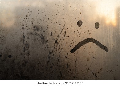 upset smiley, sad, painted on the window over a blurred background, dew and drops of water, rain, morning in the warm rays, unhappy when his rainy weather is a beautiful art. Place for inscription.