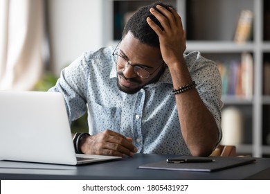 Upset stressed African American businessman using laptop, frustrated unhappy young man wearing glasses touching head, looking at screen, reading bad news in email, having problem with difficult task