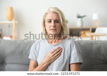 Upset stressed mature middle aged woman feeling pain ache touching chest having heart attack, sad worried senior older lady suffers from heartache at home, infarction or female heart disease concept
