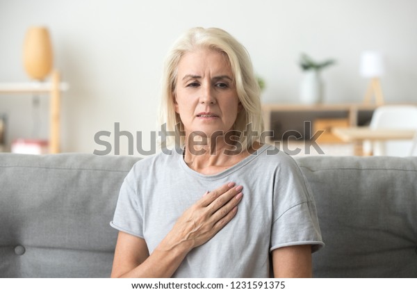 Upset stressed mature middle aged woman feeling\
pain ache touching chest having heart attack, sad worried senior\
older lady suffers from heartache at home, infarction or female\
heart disease concept