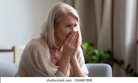 Upset stressed mature woman crying, sitting alone on couch at home, suffering from anxiety or disease, feeling lonely and unwell, desperate frustrated older female widow mourning, grieving, bad news