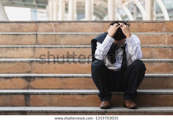 ストレスを受けたアジアの若い実業家が スーツを着て 手を階段に上げて座っている 失業とレイオフのコンセプト の写真素材 今すぐ編集
