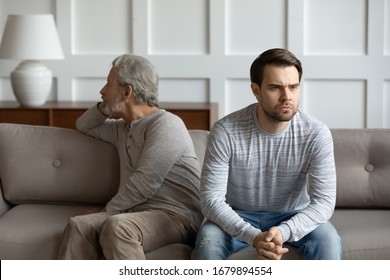 Upset Stubborn Young Man And Elderly Father Sit Separately On Couch At Home Avoid Talking After Fight, Offended Mad Mature Dad Have Misunderstanding With Adult Grown-up Son, Generation Gap Concept