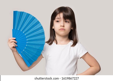 Upset Sweating Six Years Old Girl Waving Fan. Overheated Unhappy Little Preschool Cutie Suffering From Heat Stroke, High Temperature Inside Or Hot Summer Weather, Isolated On Beige Studio Background.