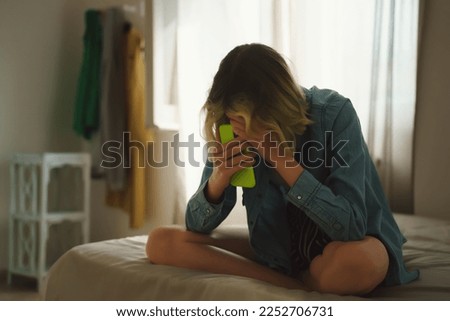 Upset teen girl on bed with phone.