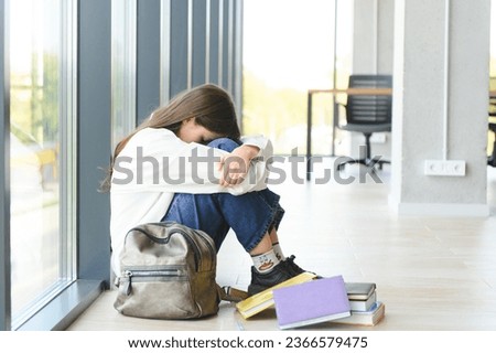 Upset teen girl sit on floor sadly look out window worried about teenage problem at school and communication with parent. Worried girl tensely suffer about bullying at school, unrequited love with boy