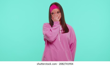 Upset Teen Stylish Girl In Pink Hoodie Making Face Palm Gesture, Feeling Bored, Shame, Disappointed In Result Of Work, Bad News. Young Woman Posing Isolated On Blue Studio Wall Background. Slow Motion