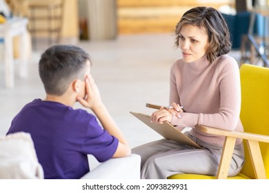 Upset teenager holding his head. Middle-aged woman psychologist talks to him. Mental health. School psychologist. Against background of light office.