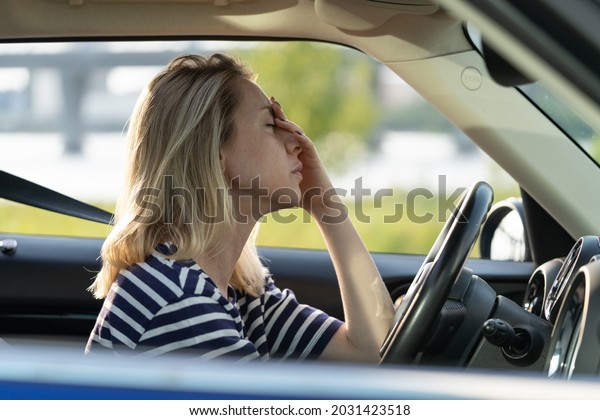 Upset or tired female driver rubbing nose and\
forehead sitting inside car driving. Middle aged woman suffering\
from headache, migraineee, panic attack or pms syndrome in vehicle\
in traffic jam on road