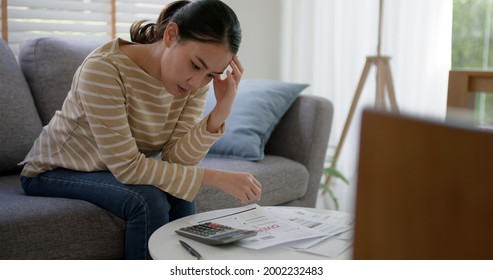 Upset tired young asia woman sit on sofa at home think hard worry in tax expense saving issue past due loan late payment on covid impact life. - Shutterstock ID 2002232483