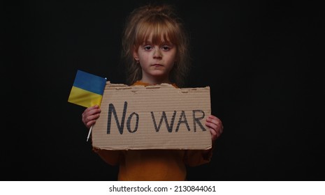 Upset Ukrainian poor toddler girl kid homeless protesting war conflict raises banner with inscription massage text No War on black background. Crisis, peace, stop aggression, child against Russian war