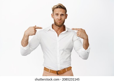 Upset And Unconfident Blond Young Man Pointing Fingers At Himself, Having Doubts, Standing In Shirt Over White Background