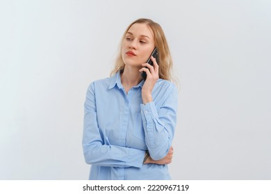 Upset And Unhappy Blonde Woman Talking On Mobile Phone, Conversation On Smartphone, Standing Over White Background In Casual Blue Shirt. Cellphone, Cellular Concept