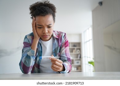 Upset Unhealthy Young African American Woman Looks At Electronic Thermometer. Biracial Teen Girl Dissapointed With High Body Temperature Covid Symptom, Suffer From Fever, Caught Cold Before Trip.