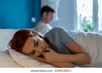 Upset wife lies with her back to husband. Frustration, unhappiness, pain, resentment and thoughtfulness on face of sad depressed woman lying in bed thinking. Man with disinterested look ignores woman. - Shutterstock ID 2344532811