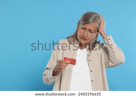 Upset woman with credit card became fraud victim on light blue background. Space for text