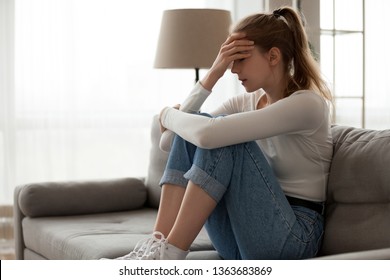 Upset Woman Frustrated By Problem With Work Or Relationships, Sitting On Couch, Embracing Knees, Covered Face In Hand, Feeling Despair And Anxiety, Loneliness, Having Psychological Trouble