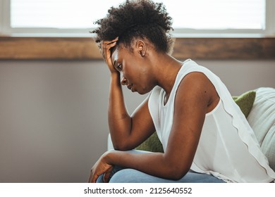 Upset woman frustrated by problem with work or relationships, sitting on couch, embracing knees, covered face in hand, feeling despair and anxiety, loneliness, having psychological trouble