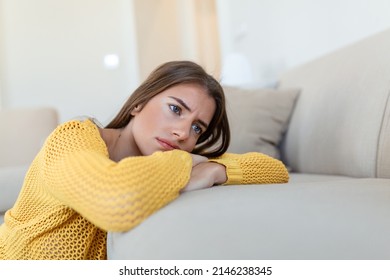 Upset woman frustrated by problem with work or relationships, sitting on couch, covered face in hand, feeling despair and anxiety, loneliness, having psychological trouble