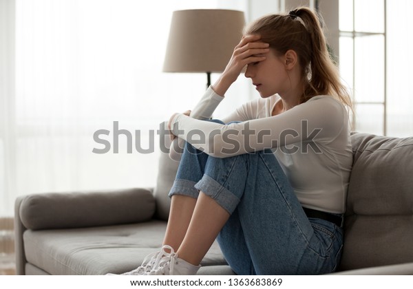 Upset\
woman frustrated by problem with work or relationships, sitting on\
couch, embracing knees, covered face in hand, feeling despair and\
anxiety, loneliness, having psychological\
trouble