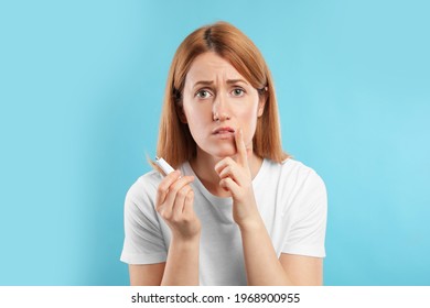 Upset Woman With Herpes Applying Cream On Lips Against Light Blue Background